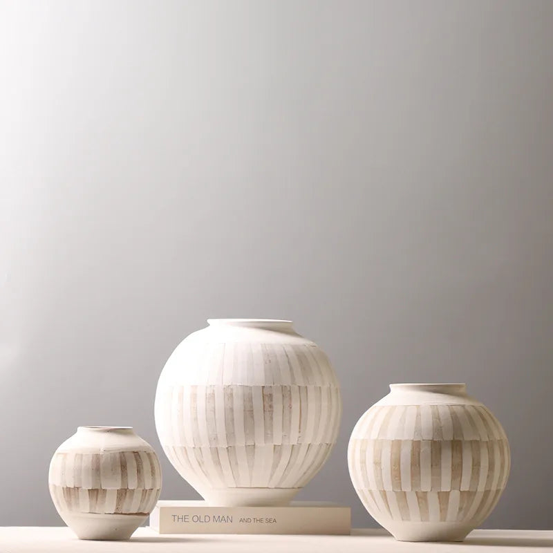 Three ribbed ceramic vases in cream and beige tones of different sizes arranged on a light surface against a soft gray background.