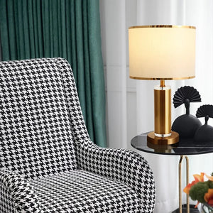 Black and white patterned chair next to a gold lamp on a side table with decorative items.
