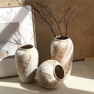 Three rustic ceramic vases with textured surfaces and dried branches on a neutral background