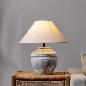 Table lamp with a textured base on a wooden side table against a gray wall.