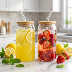 Two clear glass can-shaped tumblers with light wood lids and clear straws, shown on a plain white background.