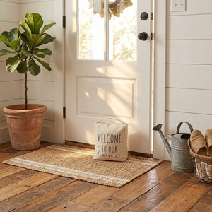 A square-shaped beige canvas door stopper with a top handle, featuring the printed phrase 'WELCOME TO OUR home' in black lettering on a plain white background.