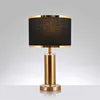 A modern table lamp featuring a cylindrical brushed gold metal base and a tapered black drum shade, shown against a plain white background.