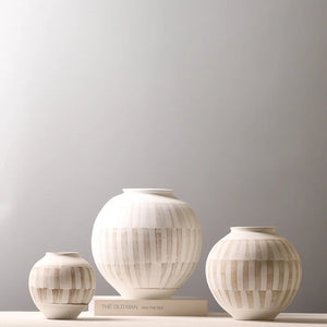 Three ribbed ceramic vases in cream and beige tones of different sizes arranged on a light surface against a soft gray background.