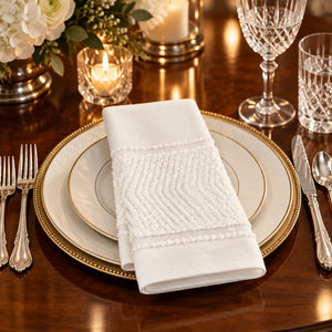 A folded white cotton hand towel with a textured chevron pattern and embroidered borders, shown on a plain white background.