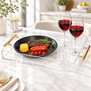 Clear acrylic serving tray with light wood and gold metal handles, shown on a white background with a black plate of food and two glasses of red wine.