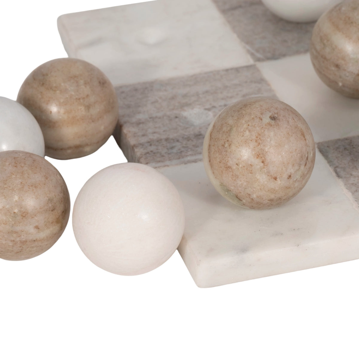 A close-up of polished marble spheres in warm beige, cream, and off-white tones arranged on and around a matching marble checkerboard against a white background.
