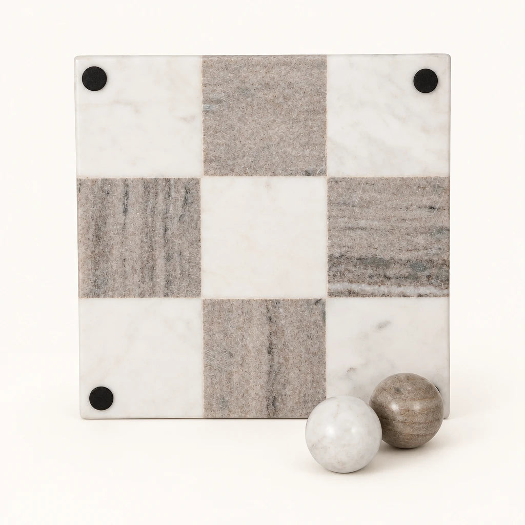 A square marble chessboard with alternating off-white and gray stone squares, shown on a plain white background with two marble balls at the bottom right.