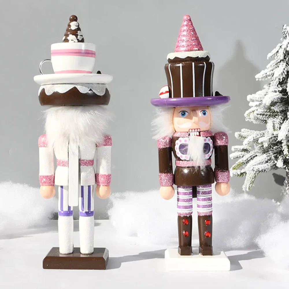 Two festive nutcracker figurines styled like decorated holiday treats, standing on a white snowy surface with a soft gray background and a blurred snow-covered tree on the right.